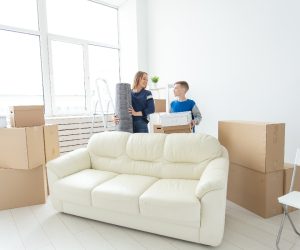 Young cute single mother and son are happy about the move to new house holding a pot of greens and carpet in their hands. Concept of housewarming and family space extensions